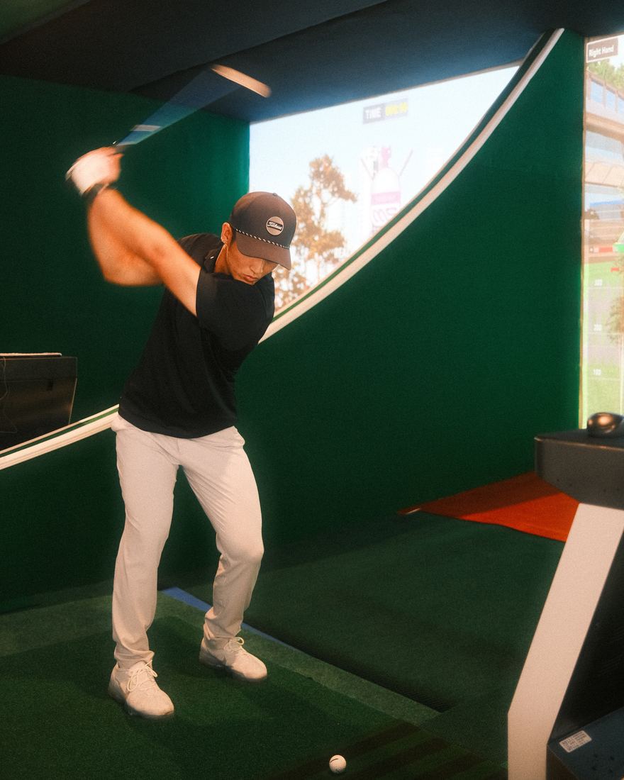 Golfer mid-swing in a simulator bay